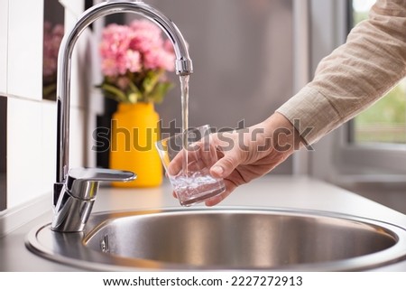 Close up of a man hand filling a glass of water directly from the tap. Filling glass of water from the tap at home.