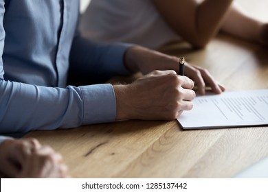 Close up of man hand holding ballpoint and signing legal document lease contract buying property. New employee affirming paper agreement with signature getting post in company human resources concept