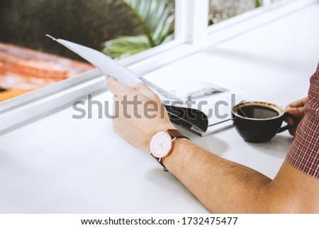 Close up of man hand holding a magazine and a cup of coffee on white table