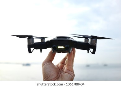 Close up of man hand holding a mini drone facing ocean, ready to be released in the sky.