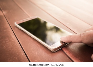Close up of man hand push /touch smart phone button on wooden table