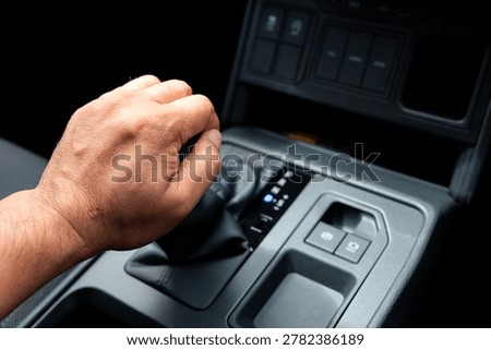 Close up of a man hand shifting the automatic gear lever stick inside a modern car interior central console panel, preparing to drive or park the vehicle, automotive transport concept.