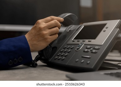 close up man hand touching telephone for call  or connecting with partner,vendor or customer at computer desktop operation room, hotline and helpline concept.