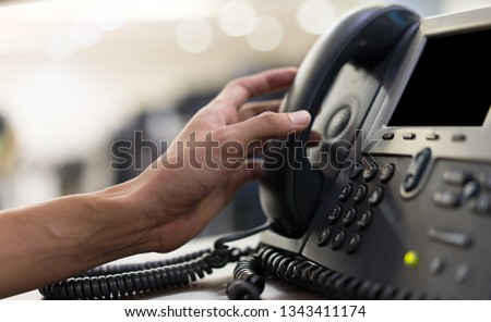 close up man hand touching telephone for call  or connecting with partner,vendor or customer at computer desktop operation room, hotline and helpline concept.