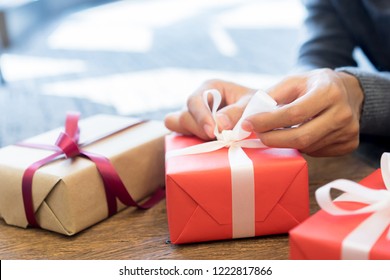 Close Up Man Hand Unwrapping On White Tied Bow On Red Box For Opening Gift At Living Room House In Merry Christmas And Happy New Year Festival Celebrate Concept