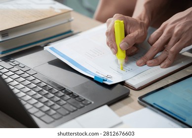Close up of a man hand using a yellow neon highlighter on a SWOT analysis document and using laptop, representing business research and academic study at home