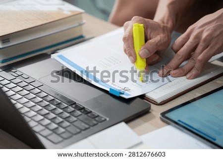 Close up of a man hand using a yellow neon highlighter on a SWOT analysis document and using laptop, representing business research and academic study at home