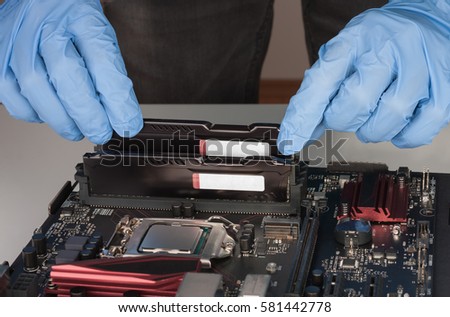 Close up of man hands with gloves installing Ram DDR4 memory module in slot on motherboard.