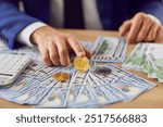 Close up of a man hands holding a Bitcoin coin amidst a pile of cash on the table, crypto financial success and the integration of cryptocurrency and traditional money in online transactions.