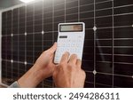 Close up of man hands holding calculator and solar panels on background. Economy and saving money by using solar energy. Energy saving, renewable energy, reduction of expenses and cheap solar energy