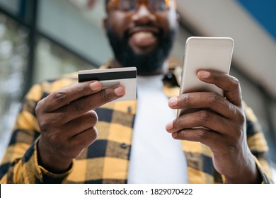 Close up of man hands holding credit card and mobile phone, shopping online. Happy African American freelancer receive payment, focus on hands