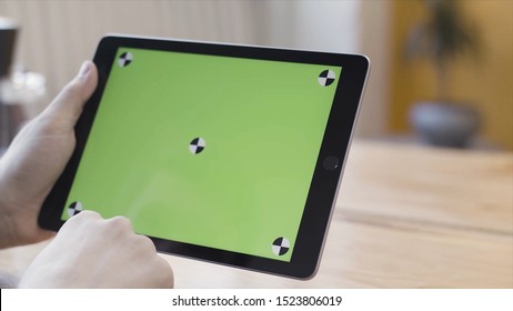 Close Up Of Man Hands Holding Digital Tablet Computer With Green Screen, Scrolling, Sliding And Tapping His Device. Stock Footage. Sitting At The Desk And Using Ipad With Chroma Key.