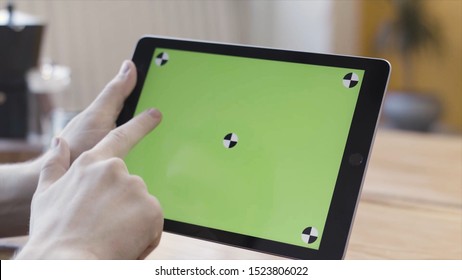 Close Up Of Man Hands Holding Digital Tablet Computer With Green Screen, Scrolling, Sliding And Tapping His Device. Stock Footage. Sitting At The Desk And Using Ipad With Chroma Key.