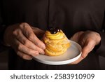 Close up of Man hands holding Italian dessert Zeppole di San Giuseppe, zeppola, fathers day pastry.  Baked puffs made from choux pastry, filled and decorated with custard cream and cherry.  