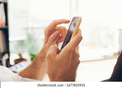 Close Up Of Man Hands Holding Mobile Phone, Using Internet While Staying At Home On Quarantine Of Corona Virus Period. Chatting With Friends And Family, Reading Latest News And  Updates In The Web.