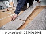 Close up of man hands laying laminate wooden planks on the floor in apartment under renovation. Male construction worker installing timber laminate flooring at home. Hardwood floor renovation concept.