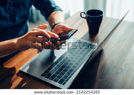 Close up of man hands with mobile phone, Businessman hand using laptop and smart phone working at home office.
