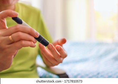 Close up of man hands using lancet on finger to check blood sugar level by Glucose meter in bedroom on the morning. Use as Medicine, diabetes, glycemia, health care and people concept.