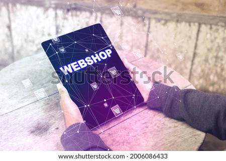 Close up of man hands using tablet with creative webshop inscription on screen. Wooden outdoor table in the background. Online shopping, e-commerce, internet purchases concept