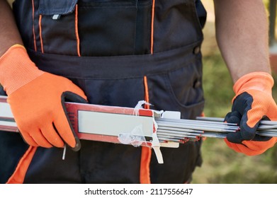 Close Up Of Man Hands In Work Gloves Holding Welding Electrodes. Male Builder With Coated Metal Wires Or Welding Rods Sticks In His Hands.