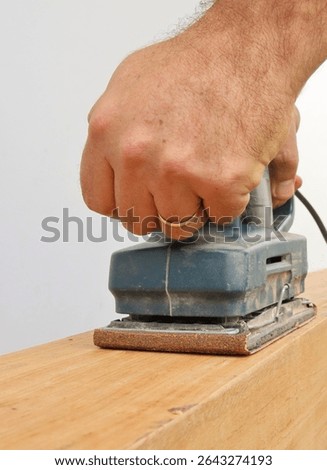 Close up of man hands working with an eletric orbital sander machine over a rustic wood. Working on costruction concept.