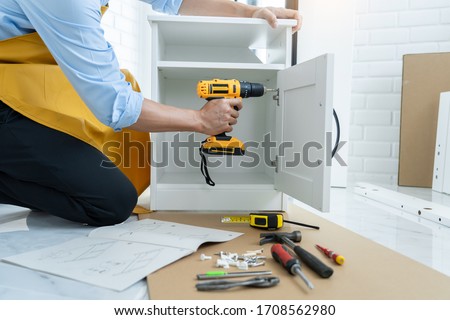 close up man holding cordless screwdriver machine and screws lie for screwing a screw assembling furniture at home