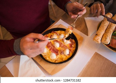 Close Up Of A Man Holding Cutlery And Eating Scrambled Eggs With Bacon At A Restaurant.