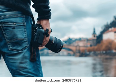 Close up of a man holding a DSLR camera with a zoom lens, standing near a body of water with a blurred background photography - Powered by Shutterstock