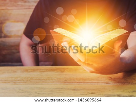 Close Up Of A Man Holding Holy Bible With Star and Bokeh Light Effected on Wood table. Copy space. Christian Background Power Of the word of God Concept.
