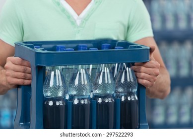 Close Up Man Holding One Dozen Of Bottled Water With No Label In A Blue Plastic Case.