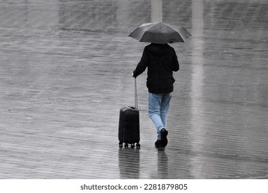 Close up man holding umbrella under rain and has suitcase walking back side and no face and reflection on ground. Rain holiday autumn concept. Selective focus. Open space area. - Powered by Shutterstock