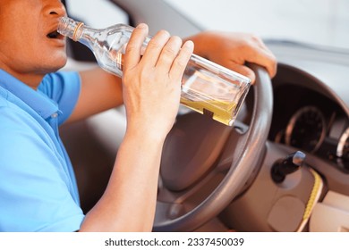 Close up man holds bottle of whiskey to drink in car. Concept , Stop driving while drinking alcohol or whiskey campaign. Illegal and dangerous to drive vehicle that leads to accident.