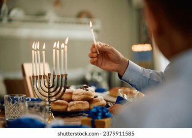 Cierre de un hombre encendiendo velas en menorah mientras celebra Hanukkah con su hijo en casa.