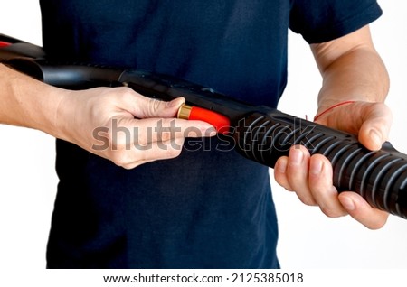 Close up of man loading a red shotgun shell into the magazine of his weapon. Charging a pump smoothbore weapon