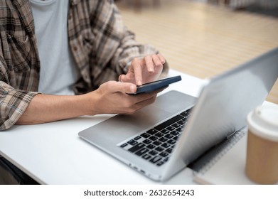 Close up of a man looking and touching on phone over laptop with coffee atop book aside sitting at cafe's white table. Study or Working, Going Outside.