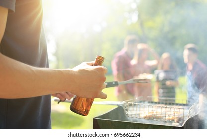 Close up of a man making barbecue and holding beer bottle.
