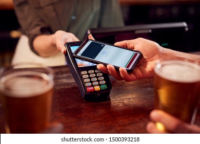 Close Up Of Man Paying For Drinks At Bar Using Contactless App On Mobile Phone