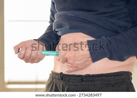 Close up of a man performing a self injection into his abdomen using a pen device, representing diabetes, migraine or weight loss treatment with modern self injection therapy.