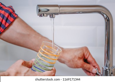 Close Up Of Man Pouring Glass Of Water From Tap With Clean Filter In Kitchen