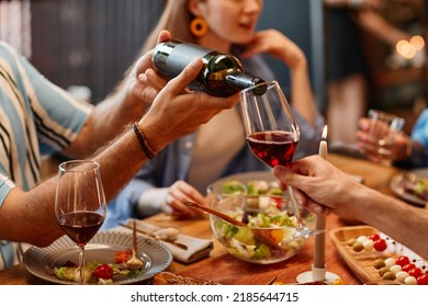 Close up of man pouring wine into glass during dinner party with cozy warm setting - Powered by Shutterstock