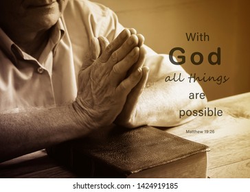 Close up of a man praying hands over holy bible on wooden table with word  from bible verses "with God all things are possible"  Christian background with copy space.