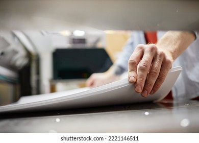 Close up of man putting stack of paper in printing machine at publishing shop, copy space