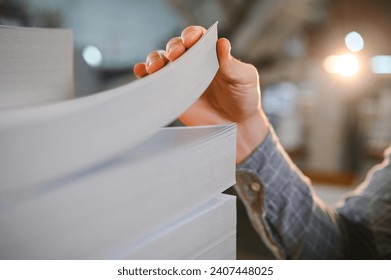 Close up of man putting stack of paper in printing machine at publishing shop, copy space.