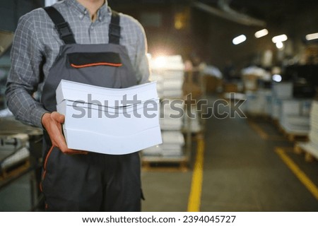 Close up of man putting stack of paper in printing machine at publishing shop, copy space.