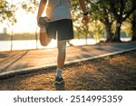 Close up - Man runner stretching leg and feet and preparing for jogging and running in public park outdoors at sunset, Active and healthy lifestyle concept, copy space