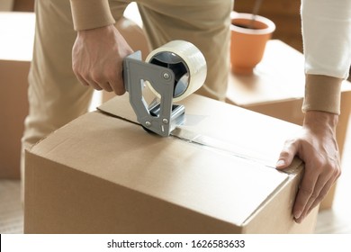 Close up of man sealing packing cardboard box with scotch tape moving or relocating, Caucasian husband roll carton package personal belongings using adhesive cellotape, relocation service concept