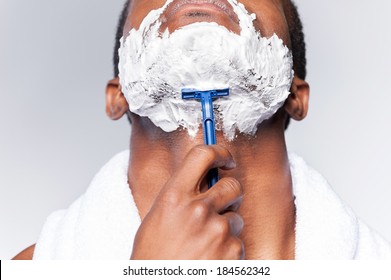 Close Up Of Man Shaving. Close Up Of Young African Man Shaving His Face While Standing Against Grey Background