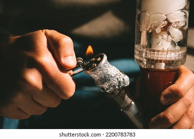 Close Up Of Man Smoking Pot Using Lighter, Medical Marijuana Or Cannabis From A Bong Or Water Pipe. Cannabis And Weed Legalisation Concept