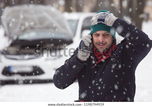 Close up of man in snow, he is under stress because\
his broken down car.