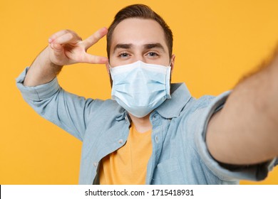 Close Up Of Man In Sterile Face Mask Isolated On Yellow Background. Epidemic Pandemic Coronavirus 2019-ncov Sars Covid-19 Flu Virus Concept. Doing Selfie Shot On Mobile Phone Showing Victory Sign